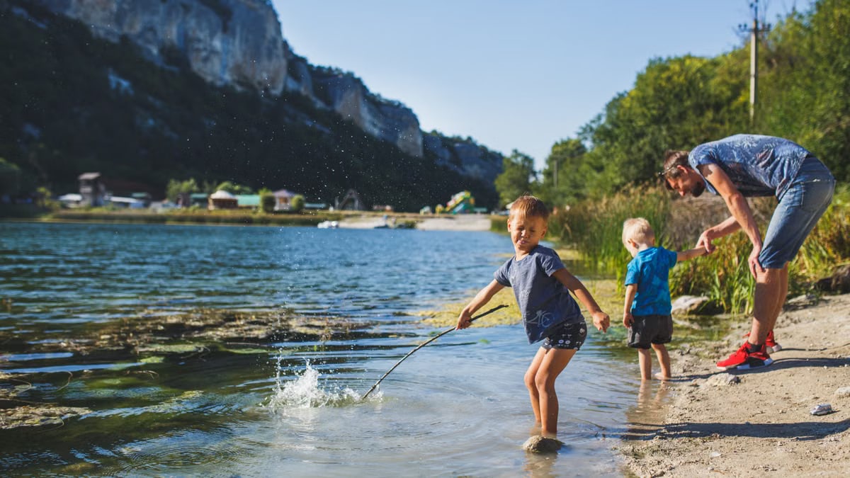 Children splashing in the lake with their father enjoying a warm sunny day outdoors.